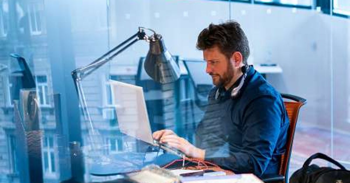 Focused male computer programmer working on laptop at desk in office